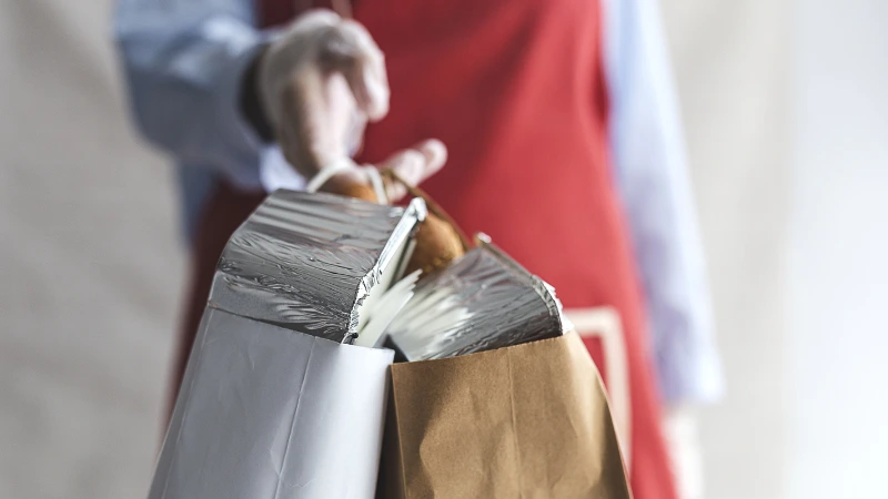 Dono de um restaurante entregando uma sacola com marmitas no delivery.