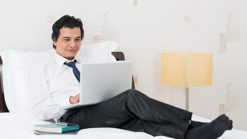 Homem trabalhando remotamente pelo notebook em seu quarto.